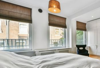 Custom dark Roman shades installed in a bright Lake Forest bedroom with three large windows